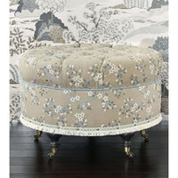 Beige poof with floral embroidery, subtle wallpaper background.