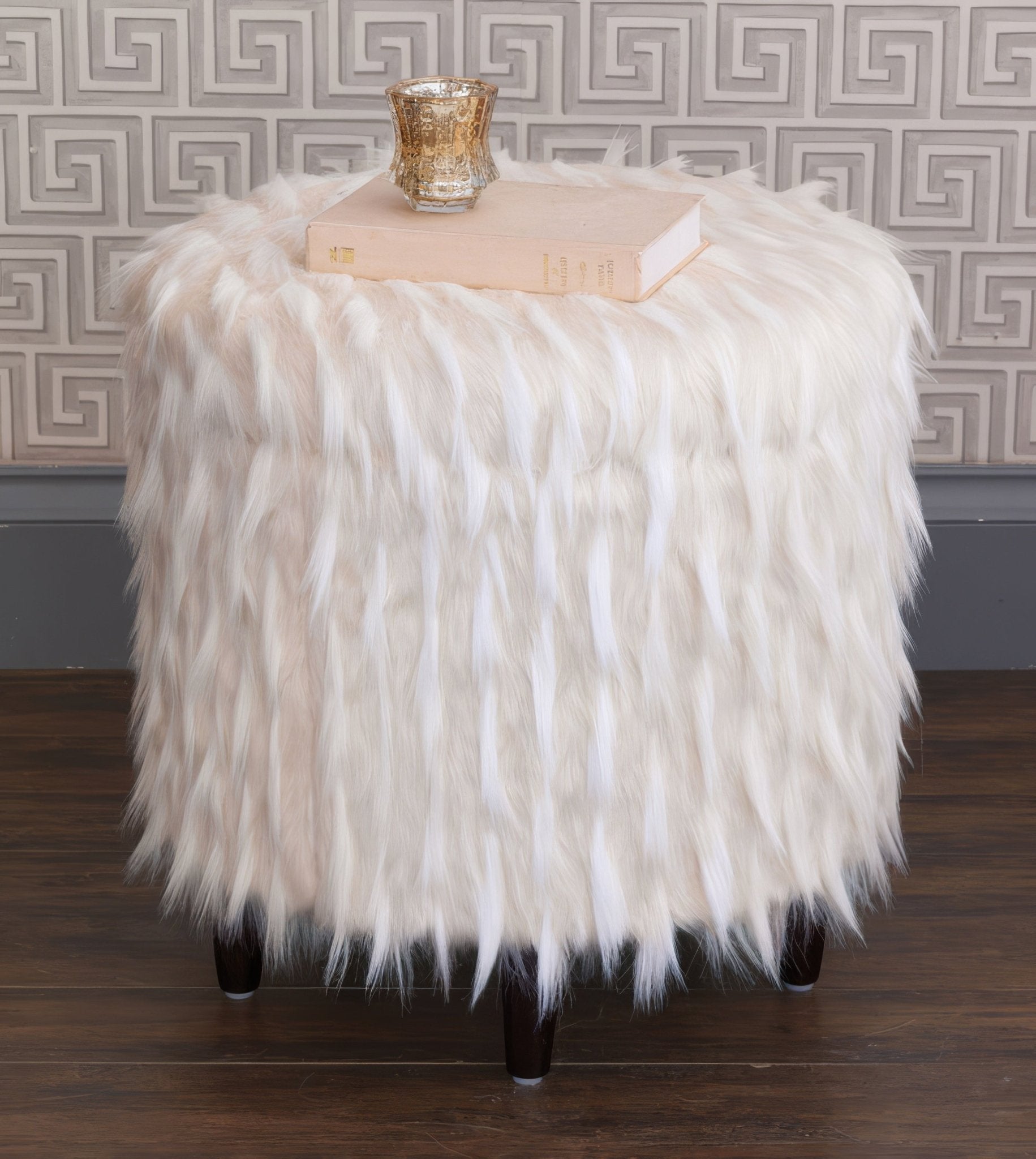 Faux fur ottoman displaying decor items on top.