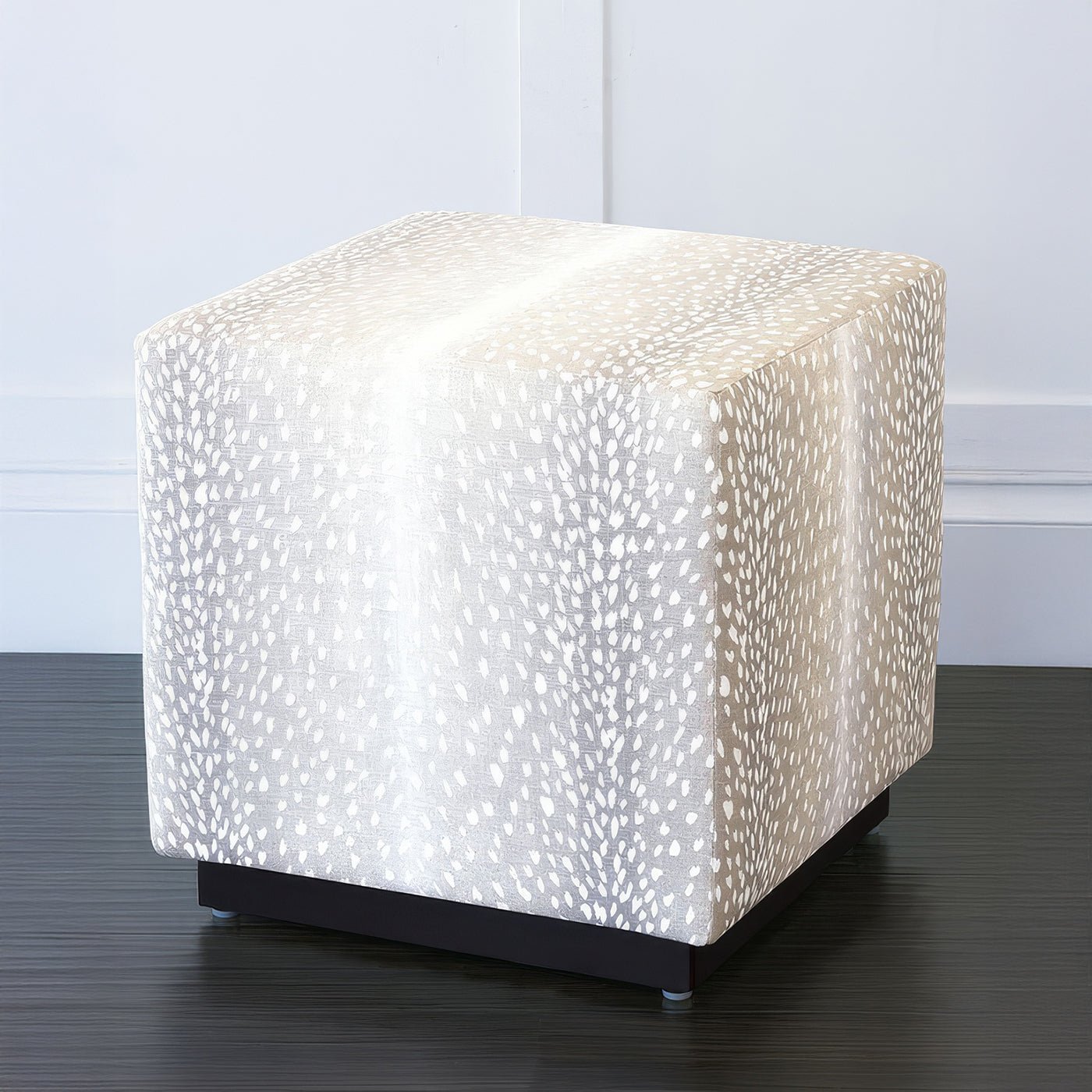 Grey cube ottoman side view near white wall.