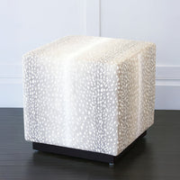 Grey cube ottoman side view near white wall.