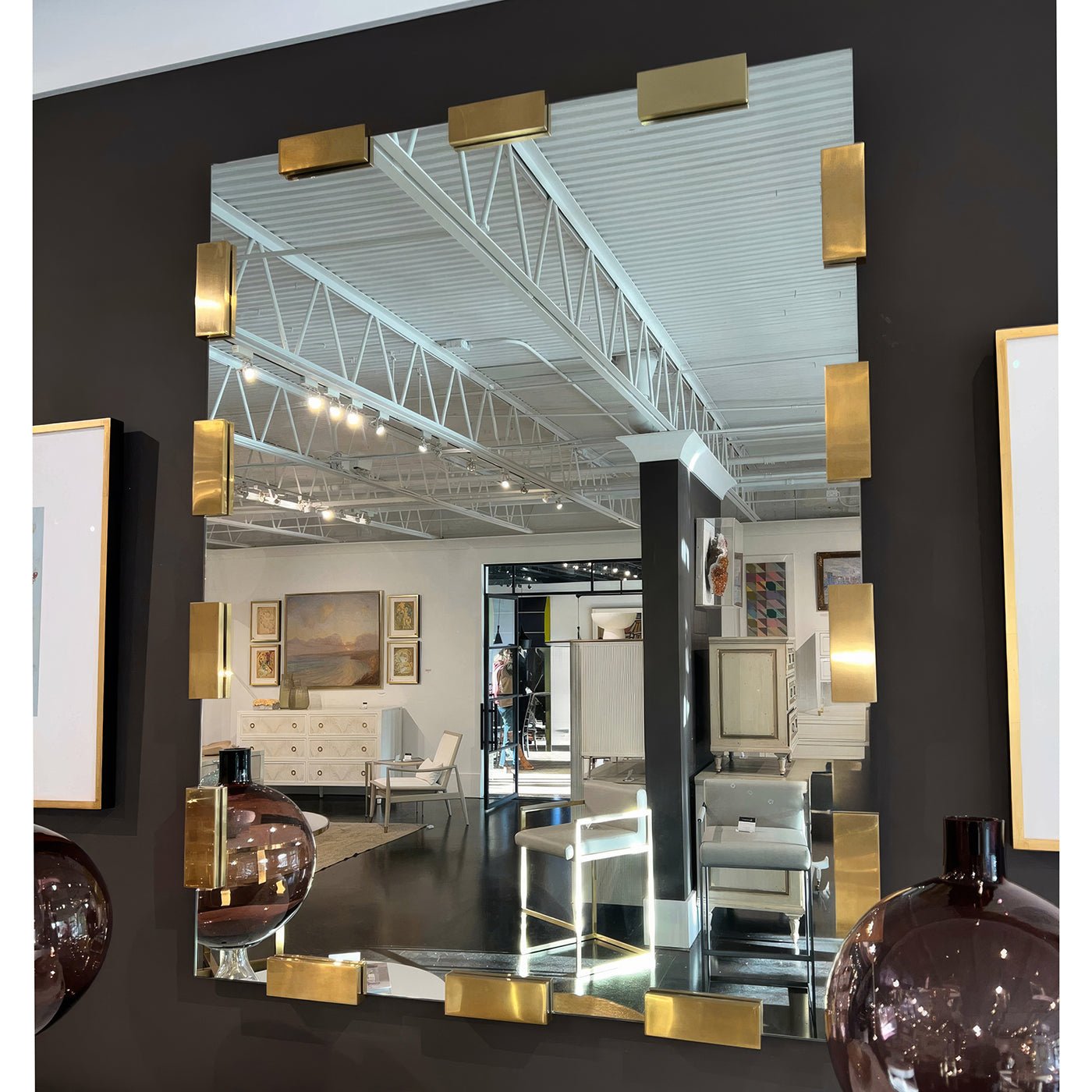 Modern mirror in gallery setting reflecting furniture and art.