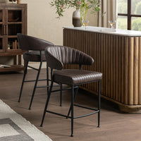Two fluted brown leather bar stools beside a wood-front bar, shown from front and rear