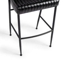 Close-up of the fluted black leather bar stool’s channel-stitched seat edge, iron legs and curved footrest