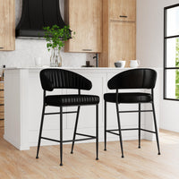 Two fluted black leather bar stools at a white kitchen island, showing the stitched front and smooth rear backrest