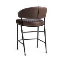 Three-quarter rear view of the fluted brown leather counter stool, showing the smooth curved back and iron footrest