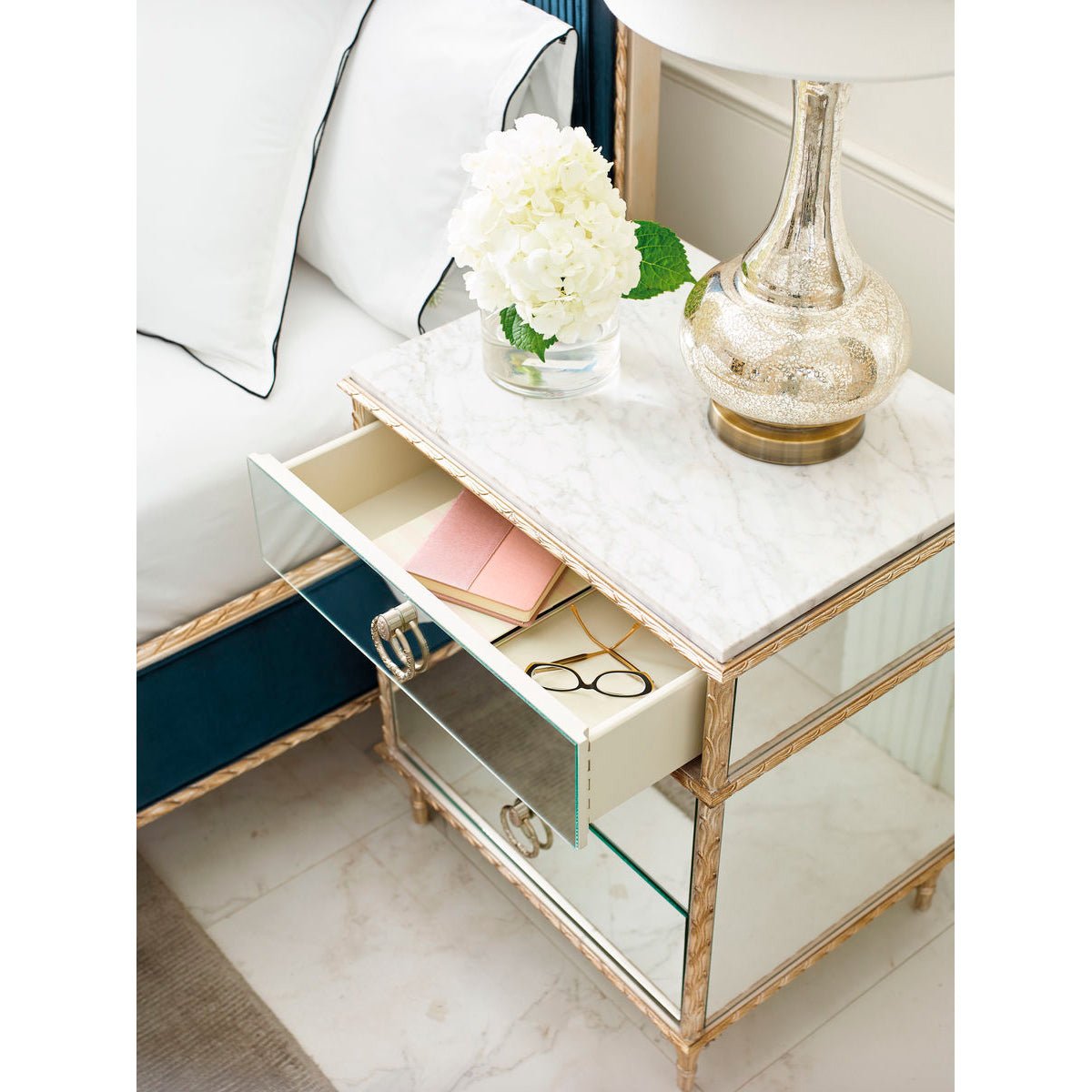 Open drawer of gold nightstand with items inside.