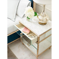 Open drawer of gold nightstand with items inside.
