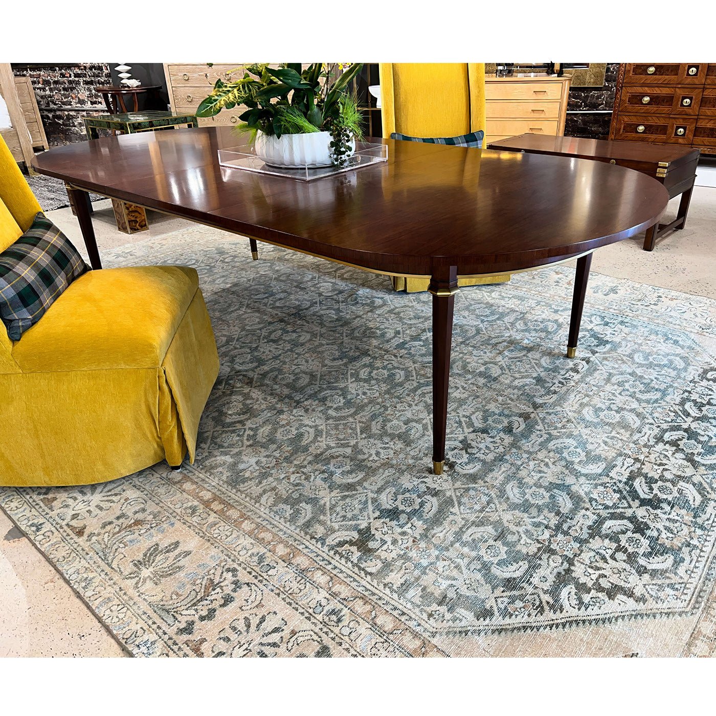 French walnut dining table on patterned rug with yellow chairs.
