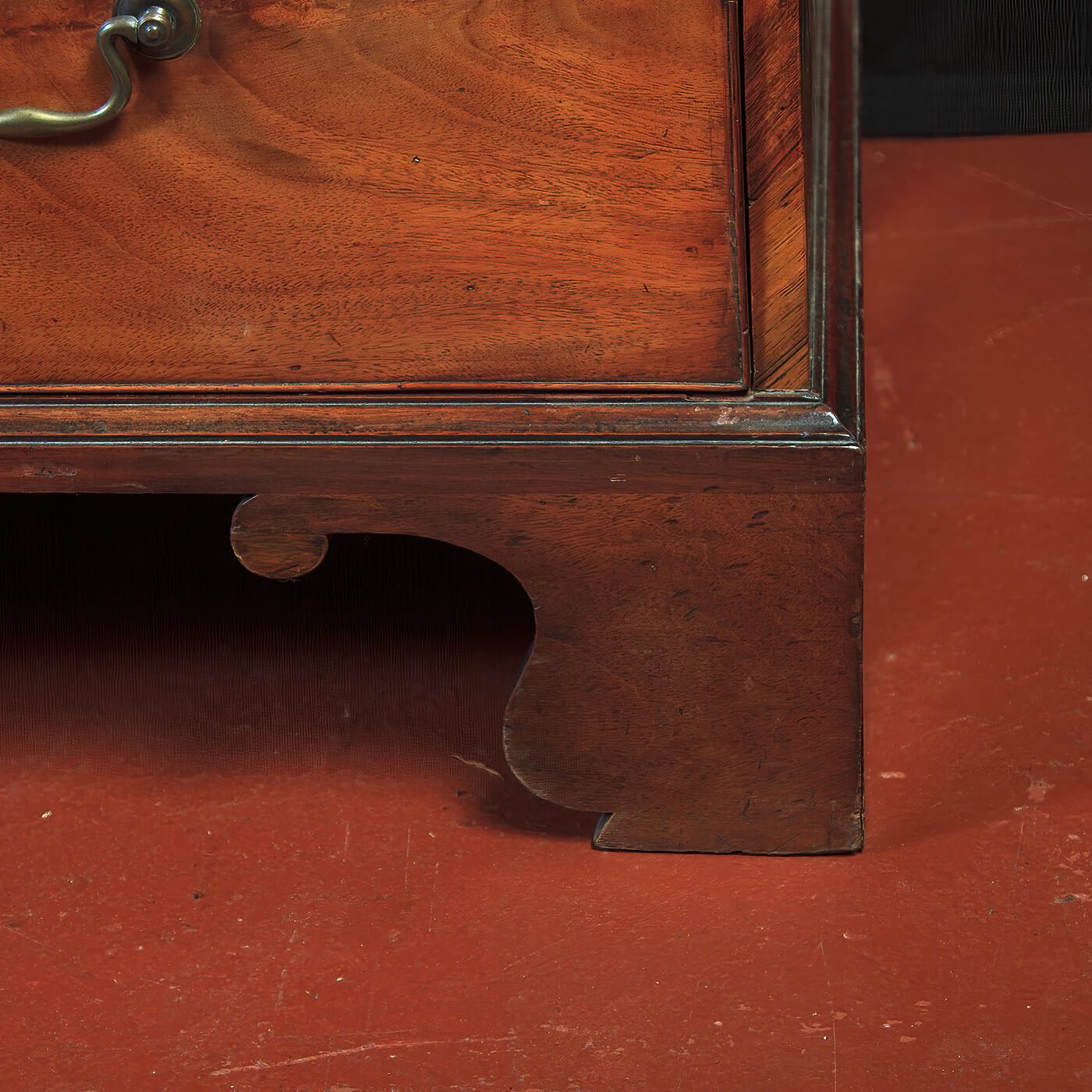 Base detail of mahogany chest on reddish floor.