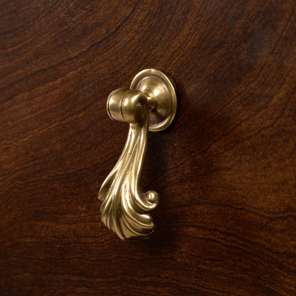 Close-up of brass handle on mahogany chest drawer.