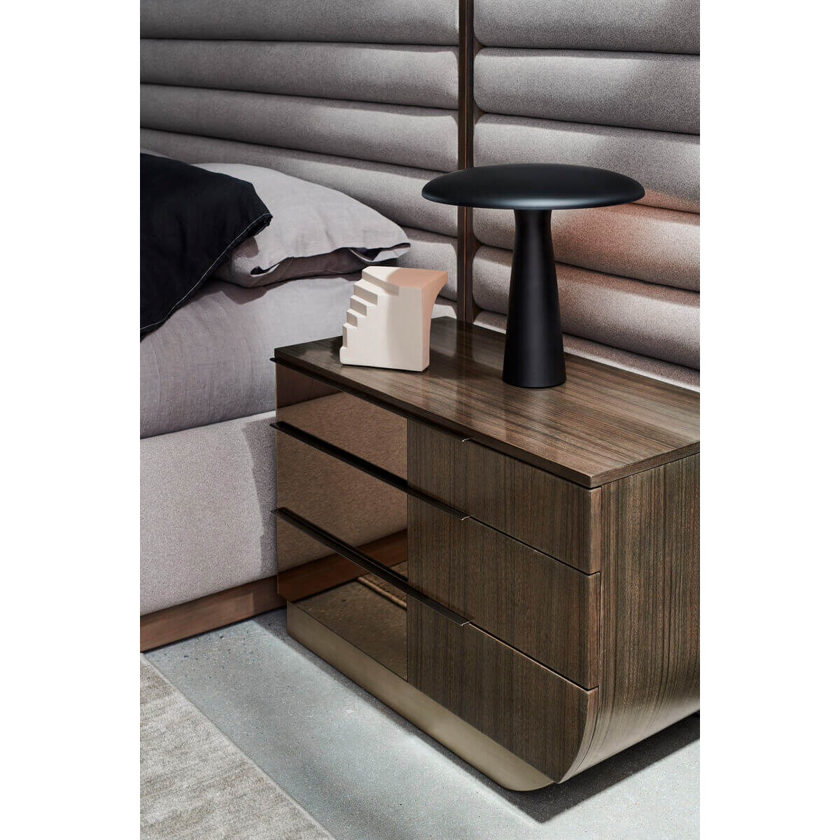 Nightstand next to gray channeled king bed with decor.
