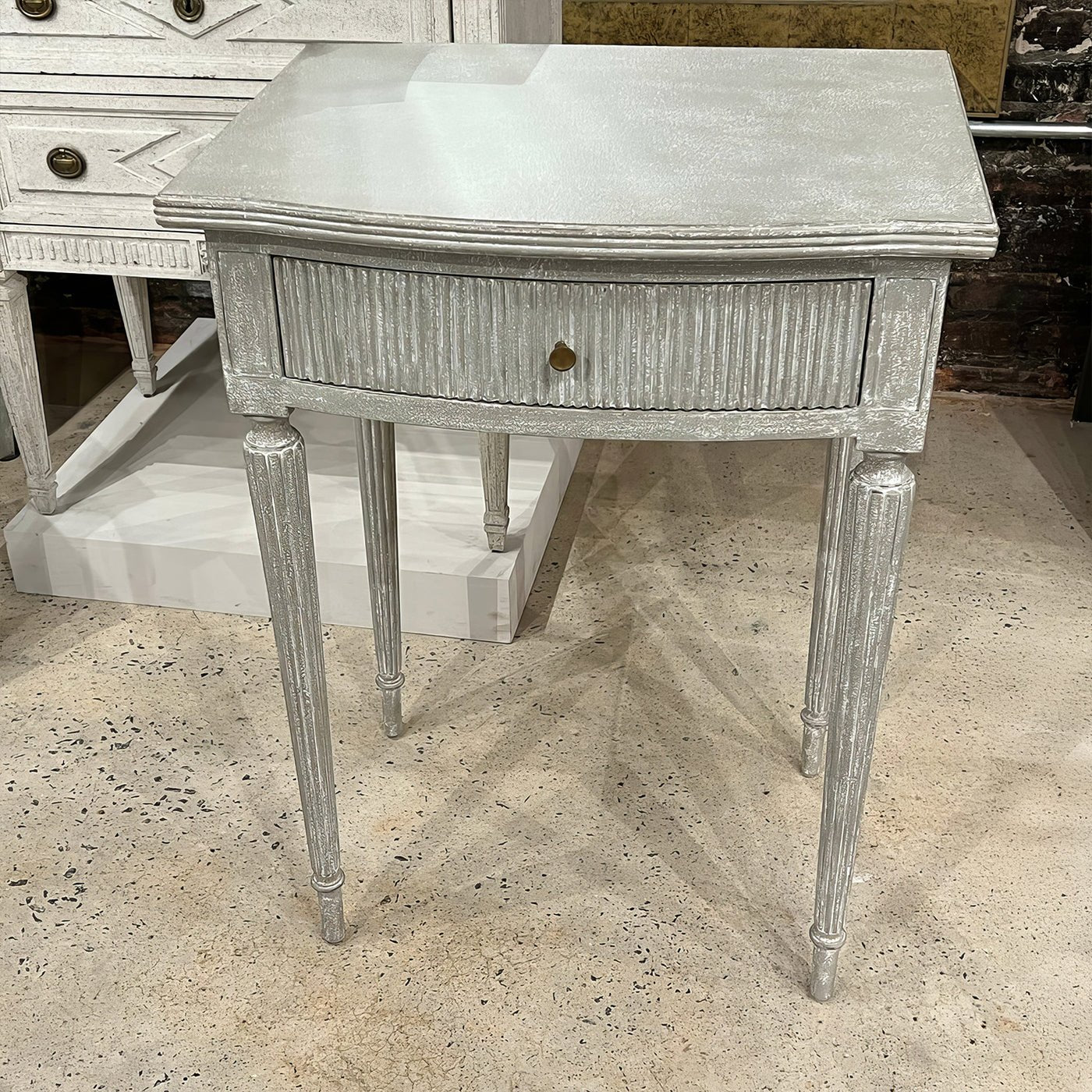 Gray Gustavian side table on textured concrete floor.