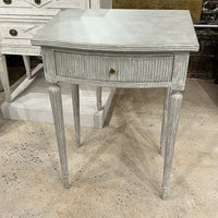 Gray Gustavian side table on textured concrete floor.