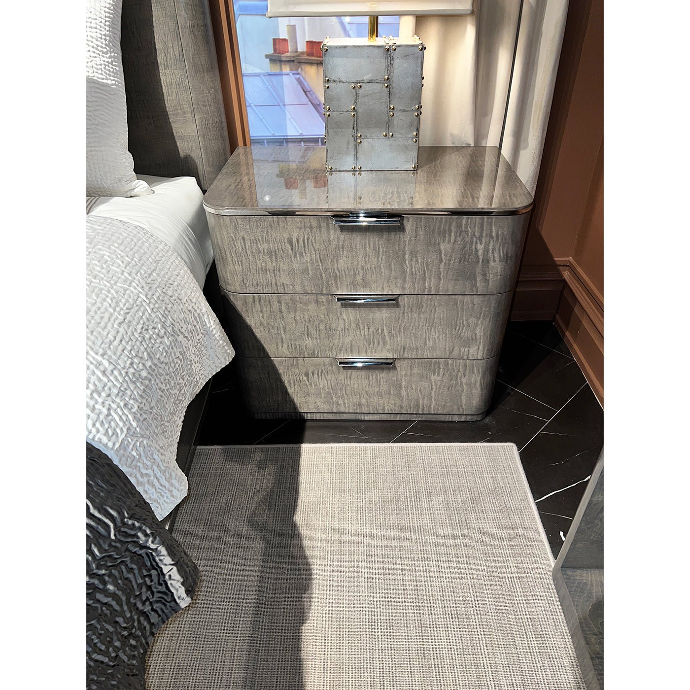 Grey Art Deco nightstand beside bed, decorative items on top