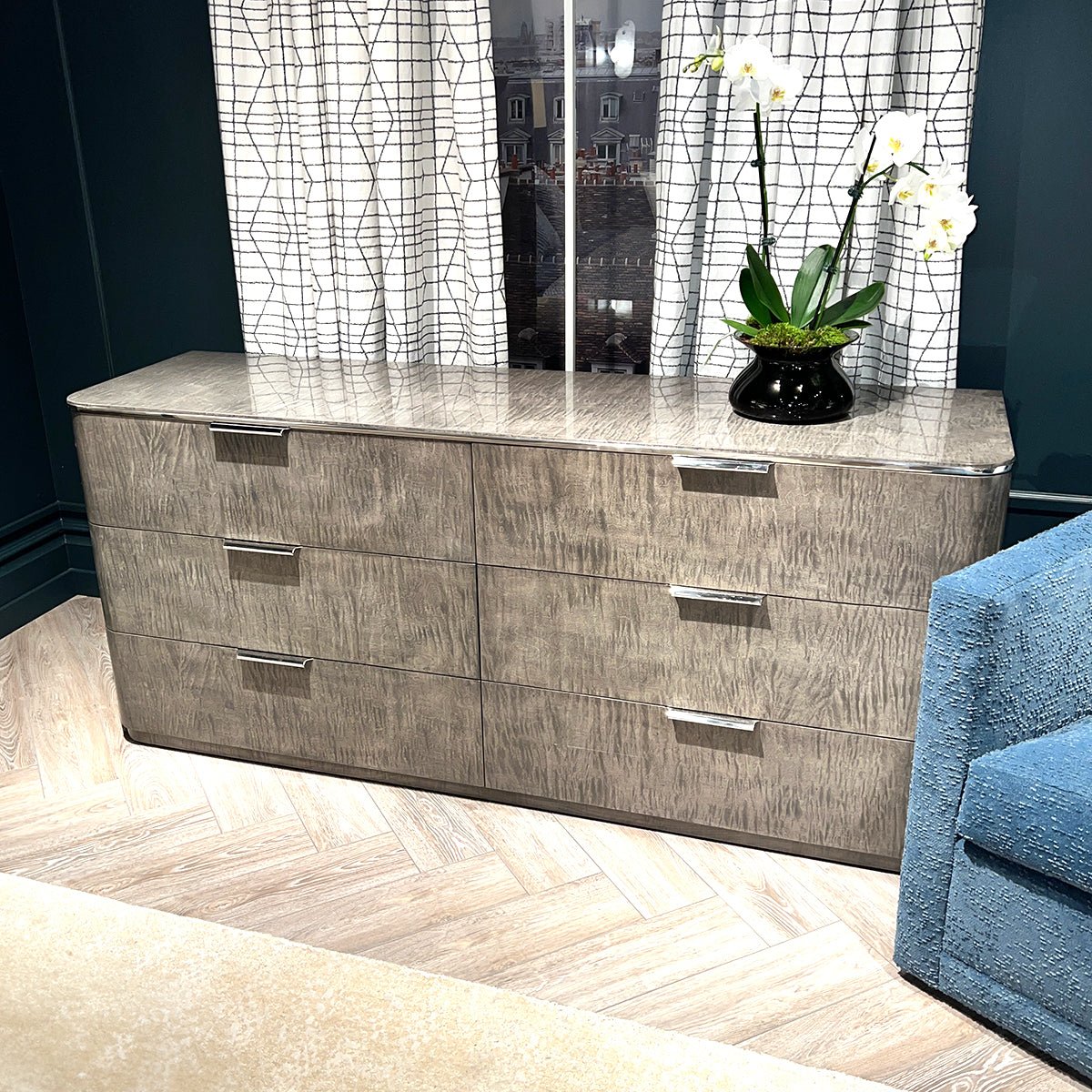 Dresser in room with flower vase, blue chair visible.