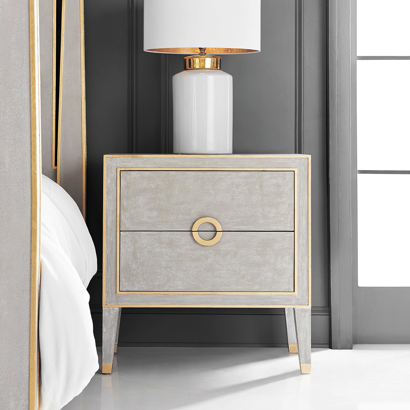 Nightstand by bed with lamp, grey and gold design.