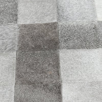 Close-up of the Sparrow Gray bench upholstery showing gray and white hair-on-hide patchwork seams