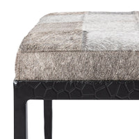 Close-up of the Sparrow Gray bench showing hair-on-hide patchwork, stitched seat edge and textured iron apron