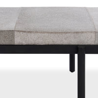Close-up of the gray hair-on-hide bench seat, patchwork seams and black iron frame with round legs