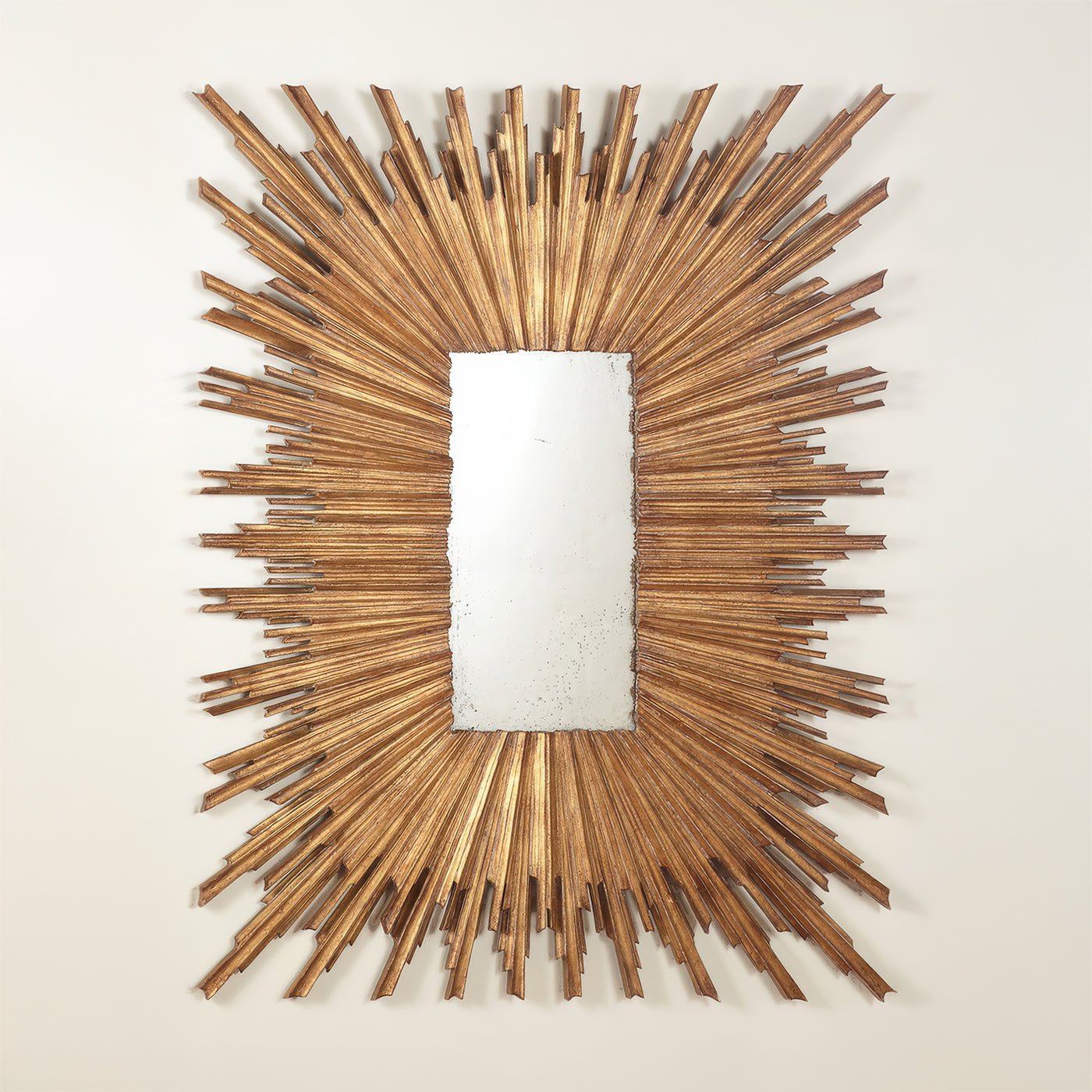 Gold sunburst mirror on white wall, front view.