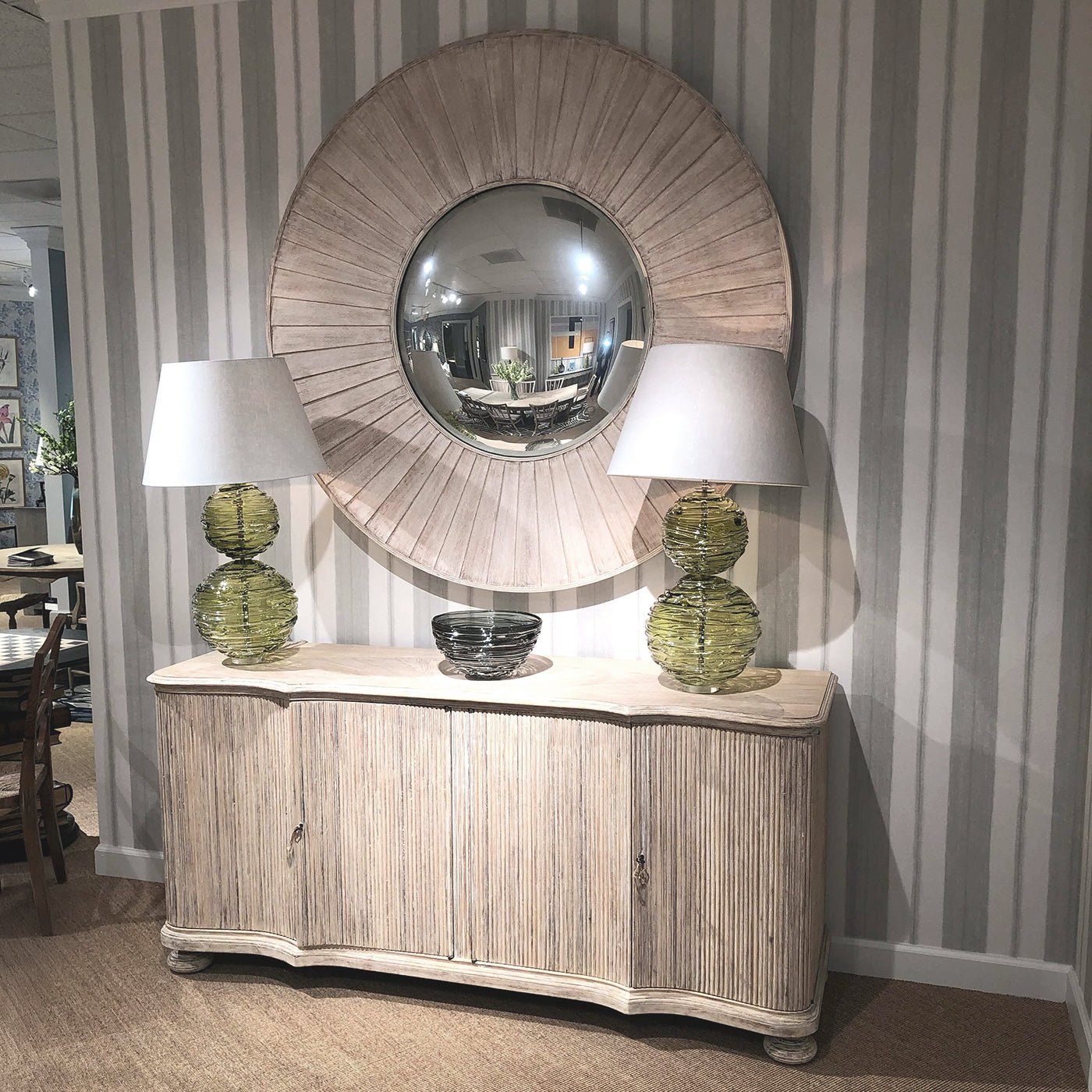 Large round mirror above cabinet, flanked by lamps.