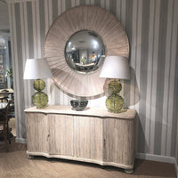 Large round mirror above cabinet, flanked by lamps.
