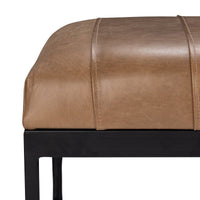 Close-up of the brown leather bench showing stitched seat channels, a rounded cushion edge and black iron apron