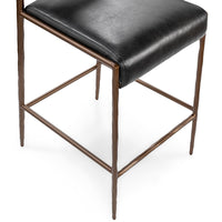 Detail of the black padded seat above the bronze-toned iron legs and wraparound footrest