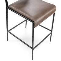 Detail of the taupe padded seat above the dark hammered iron legs and wraparound footrest