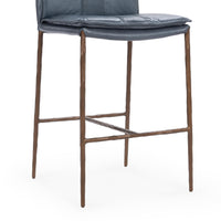 Close-up of the slim-frame blue leather counter stool’s padded seat edge, brown iron legs and footrest