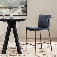 Slim-frame blue leather counter stool beside a round black table on a patterned rug