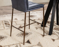 Rear-side detail of the blue leather counter stool’s brown iron legs and footrest beside a black table
