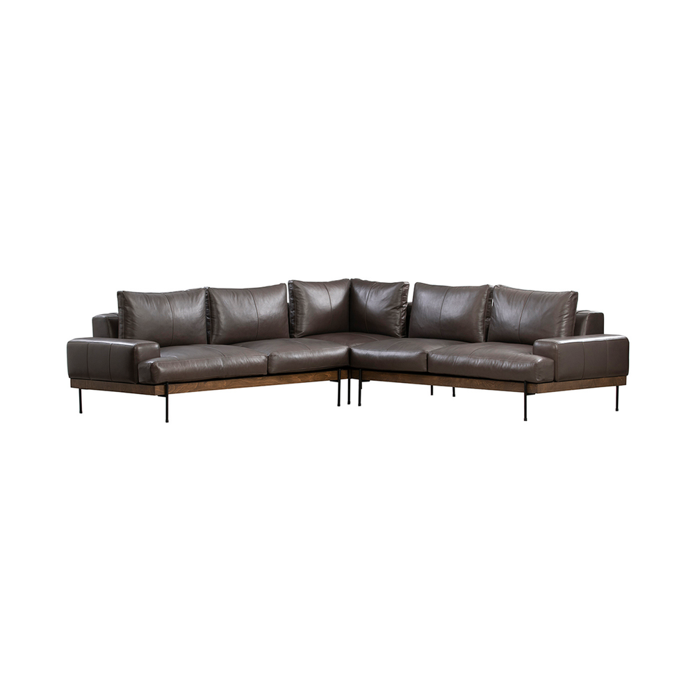 Front corner view of brown three-piece leather sectional with padded arms, a wood rail and slim dark legs