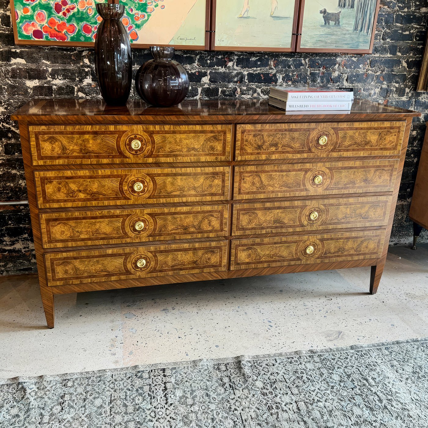 Louis XVI burl dresser near art-covered brick wall.