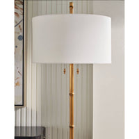 White shade on gold floor lamp against textured wall.