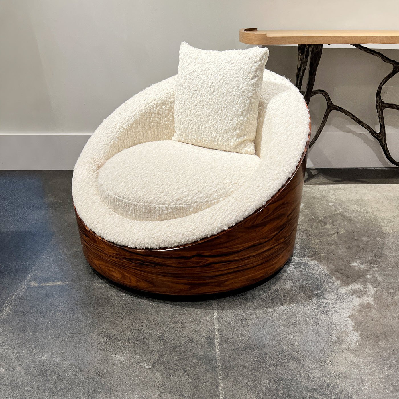 Lounge chair on gray floor, white pillow, wood base.
