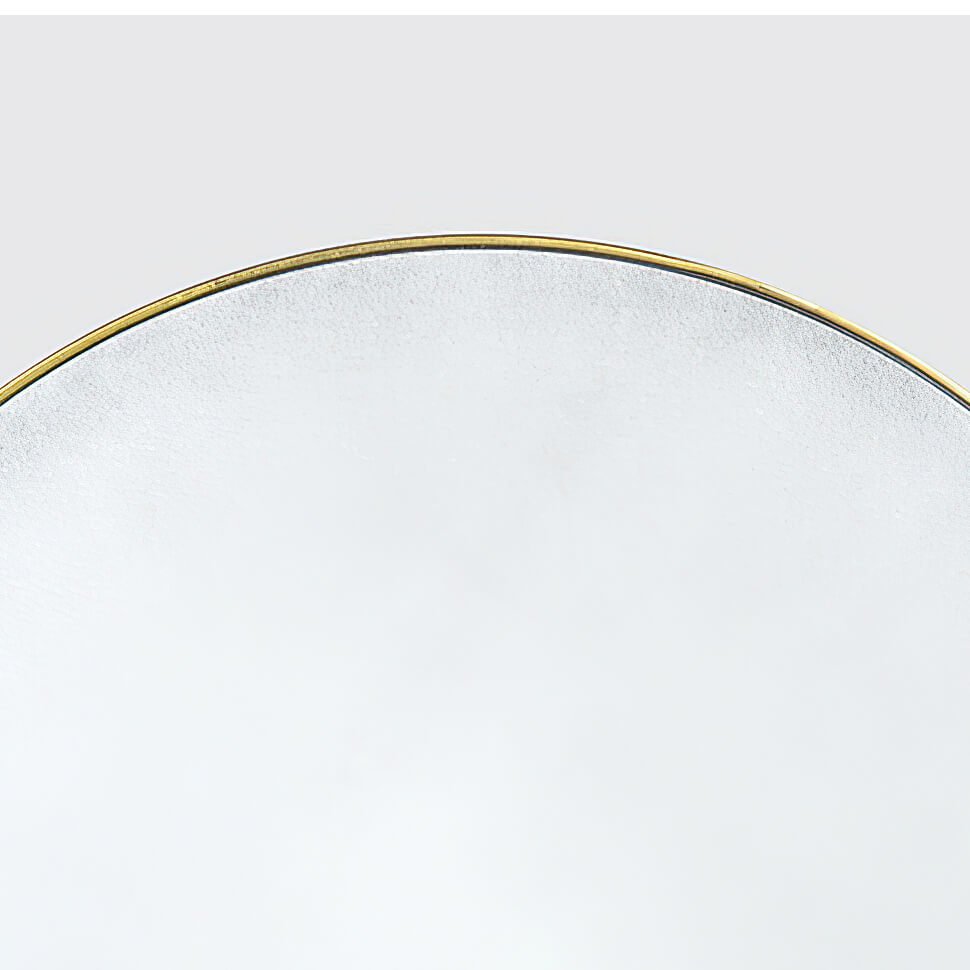 Edge of circular mirror with gilt frame detail.