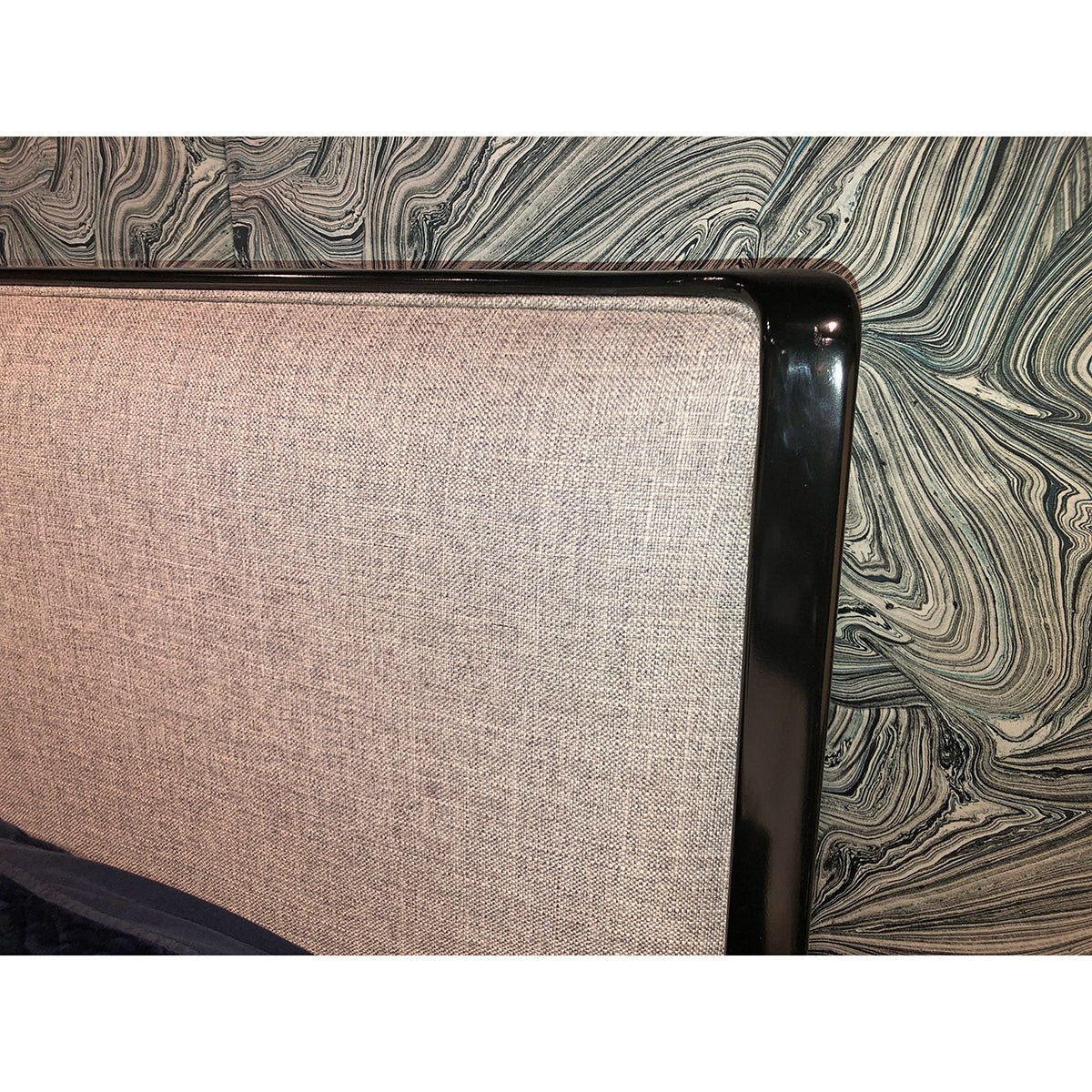 Detailed view of textured headboard against patterned wallpaper.