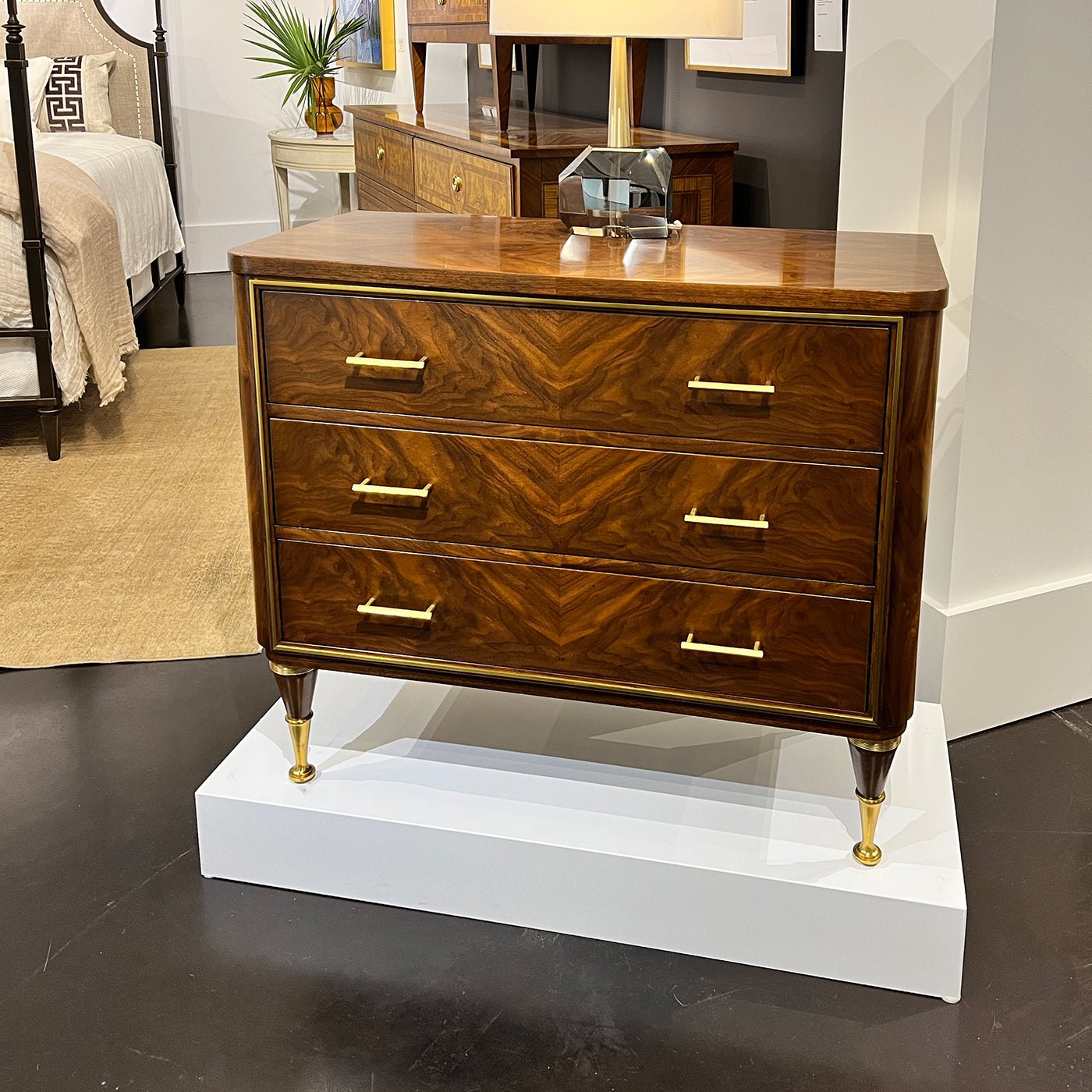Walnut bedside chest on display pedestal, showroom setting.