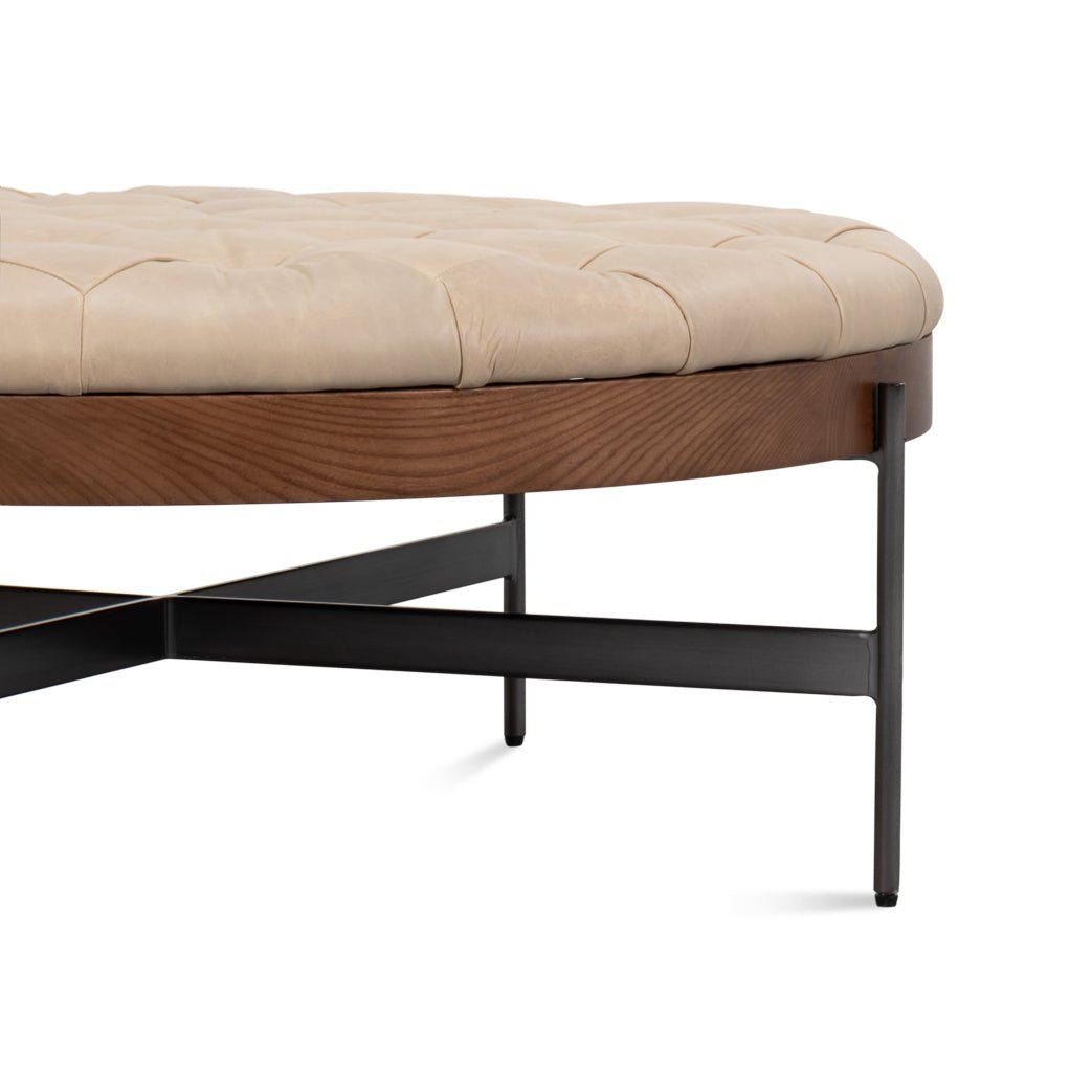 Side close-up of ottoman showing tufted surface and frame.