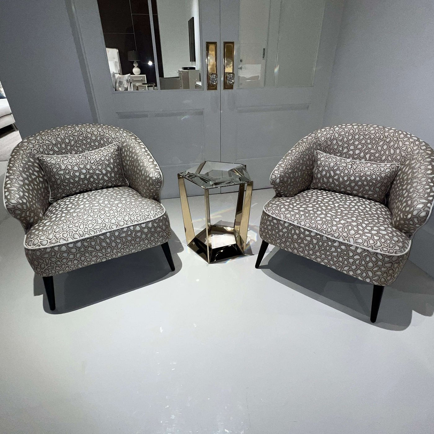 Accent table with glass top between patterned armchairs.