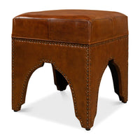 Angled view of leather ottoman, rivet-studded arch base.