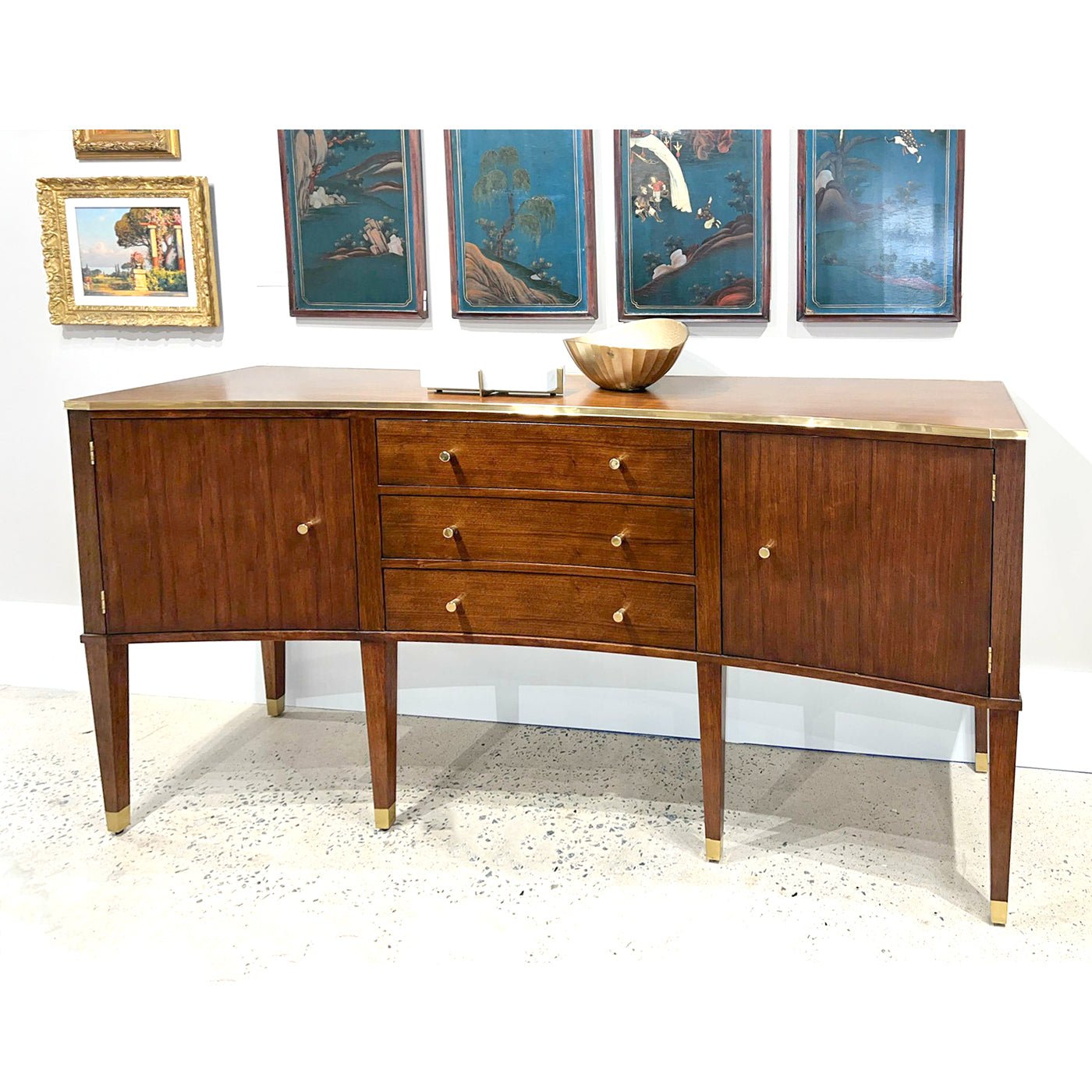 Modern walnut sideboard in room, decorated with artwork and bowl.