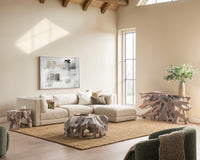 Beige modular seating in a sunlit living room with sculptural wood tables and a woven rug