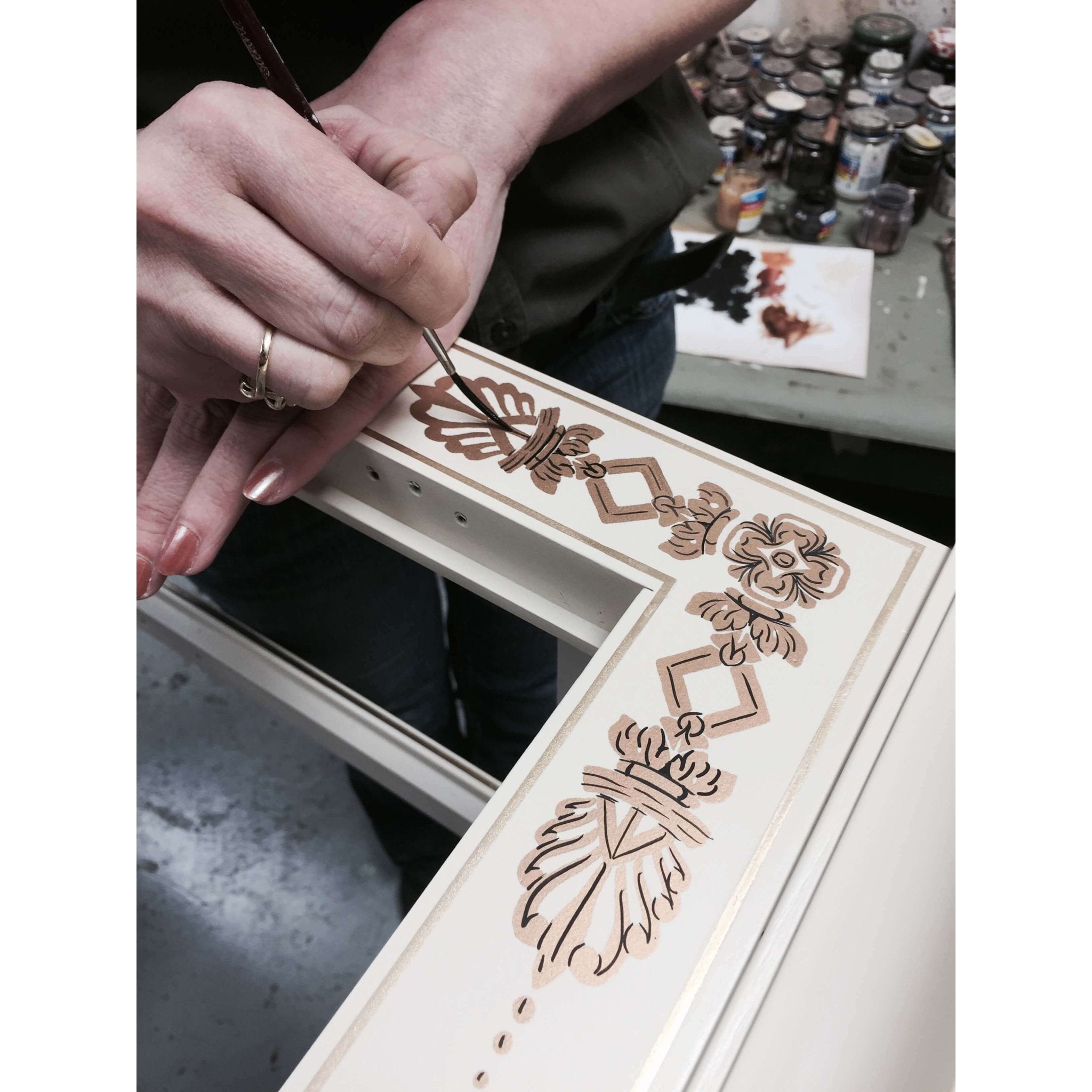 Hand-painting intricate designs on cabinet surface.