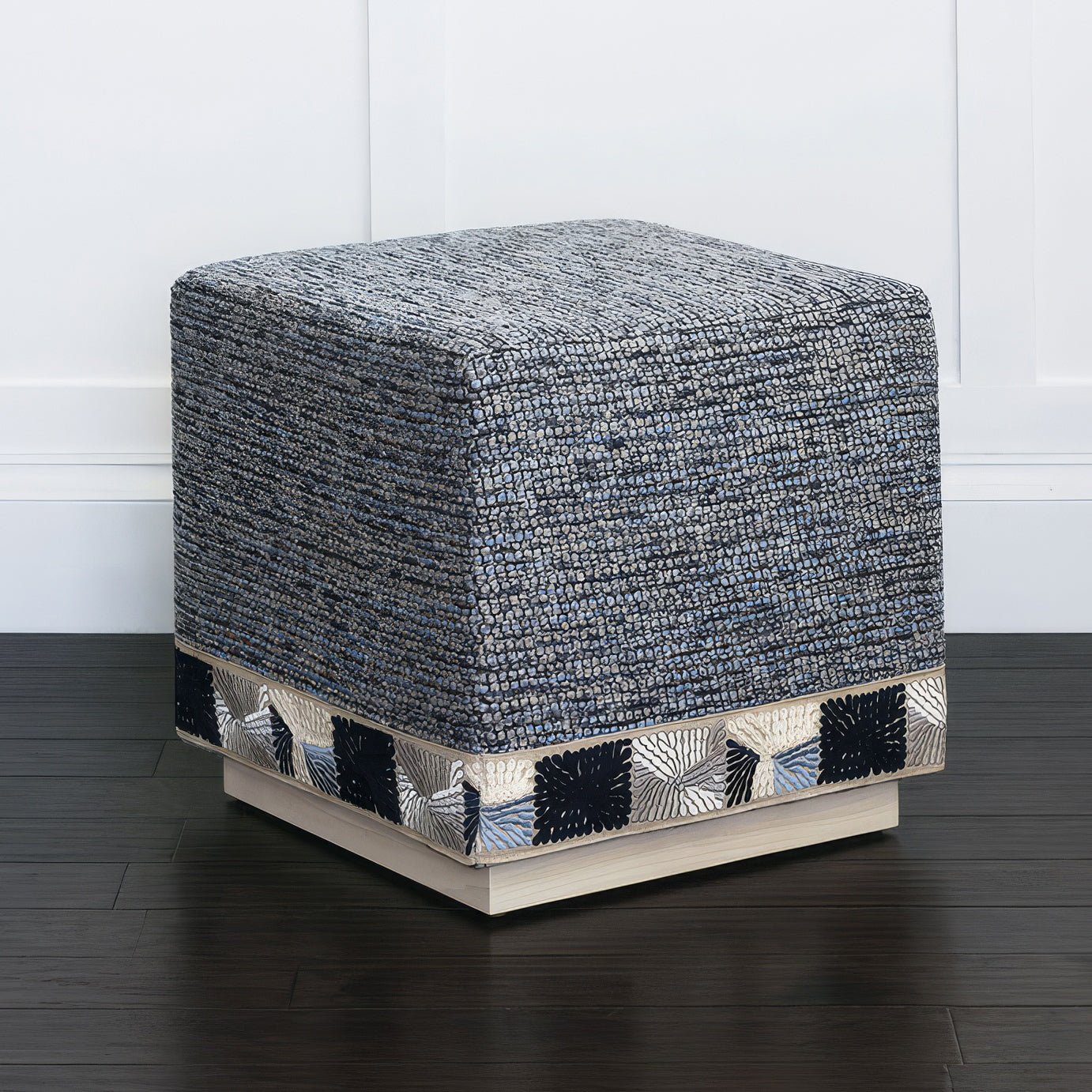 Blue ottoman in a room, dark floor, wall background.