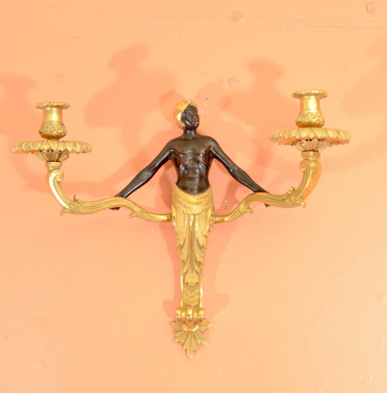 Single Louis XV bronze sconce, orange wall backdrop.