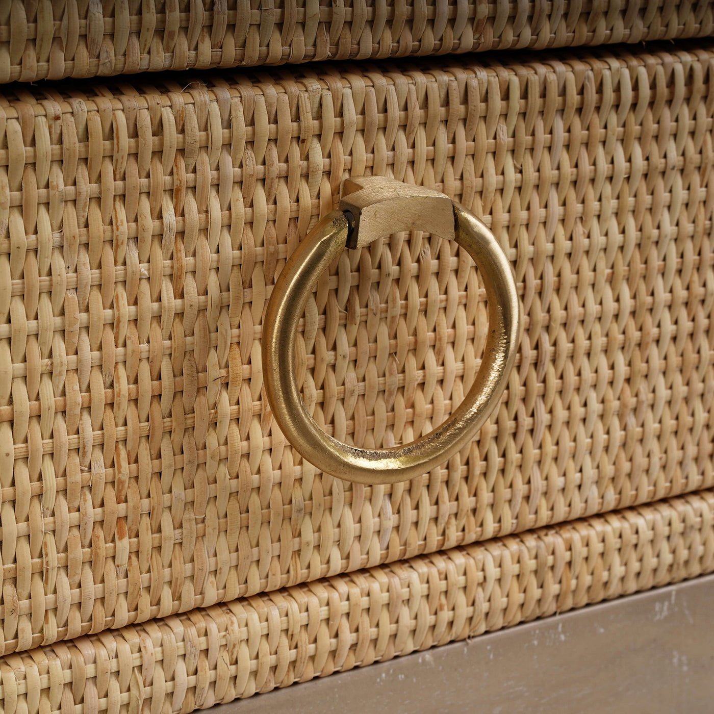 Close-up of nightstand brass ring handle and rattan texture.