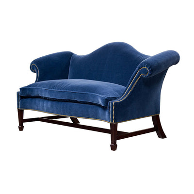 Blue camelback sofa with wooden legs angled view.