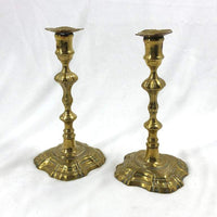 Two ornate Queen Anne brass candlesticks, side view.